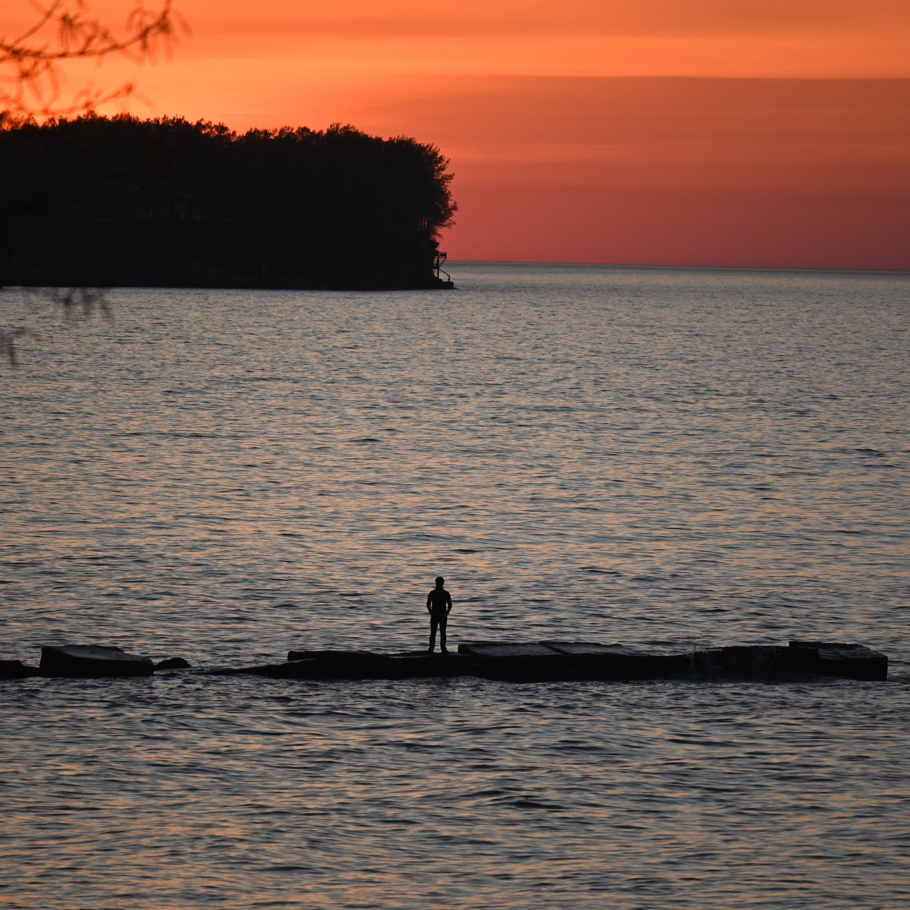 A person watching the sun set on a rocky pier.